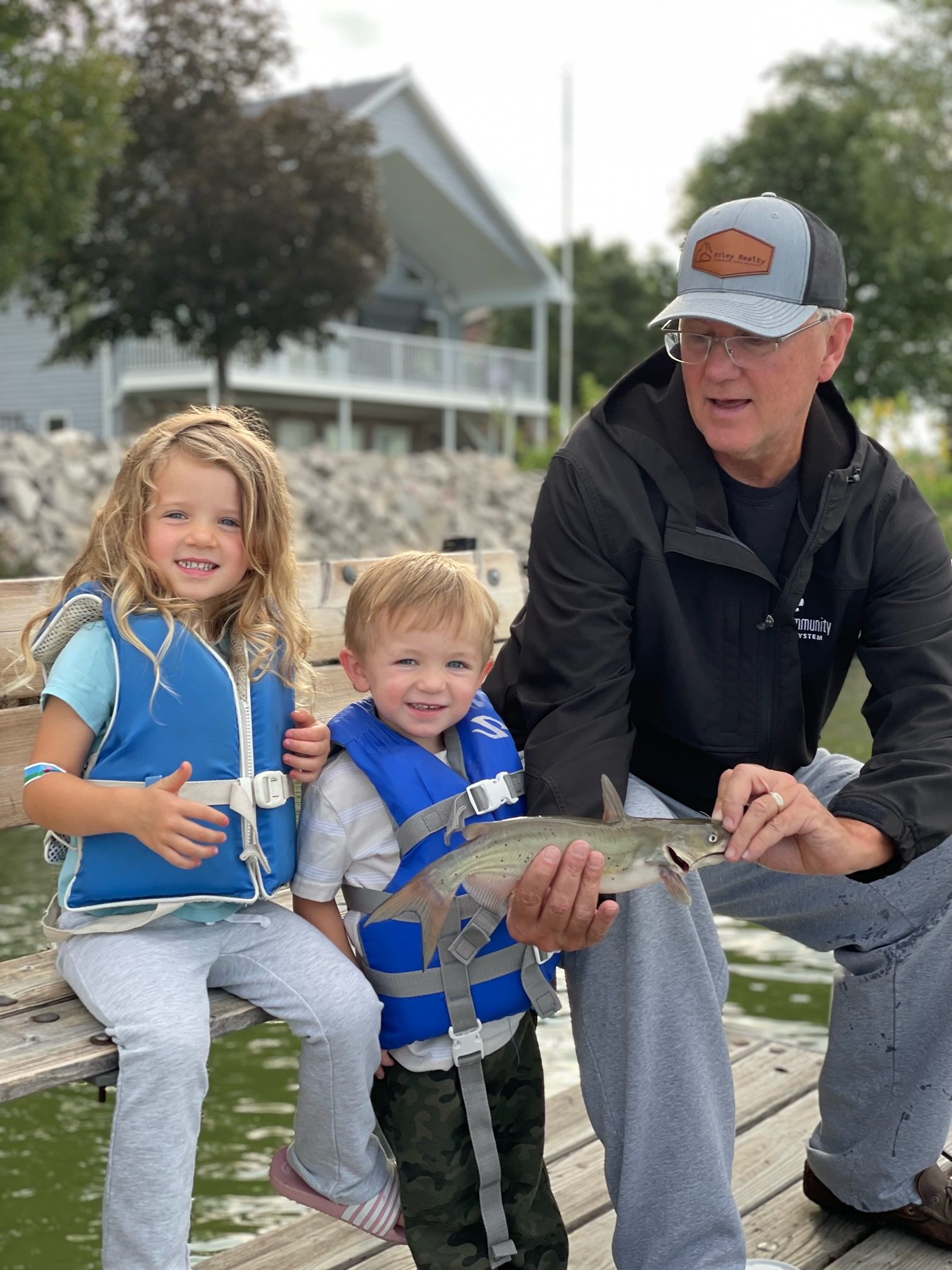 Kirk Riley and two grandkids on a bench holding fish