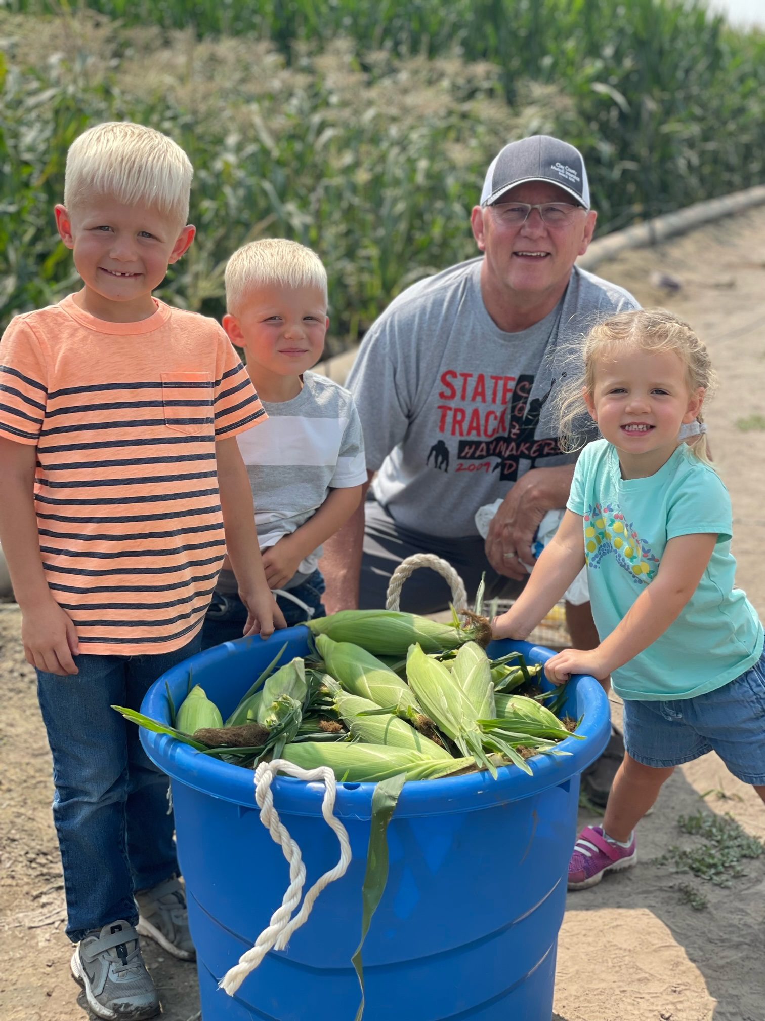 Kirk Riley with grandkids around a bucket with corn